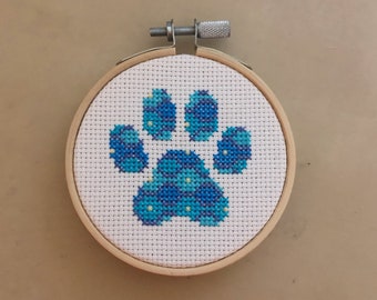 May include: A blue and white paw print cross-stitch design in a wooden embroidery hoop.