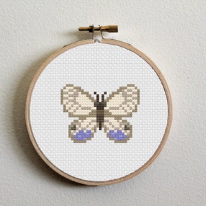 May include: A white butterfly with purple accents is embroidered on a white canvas, framed in a wooden hoop.