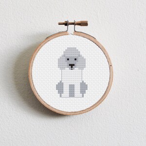 May include: A white and grey cross-stitch embroidery of a poodle in a wooden embroidery hoop.