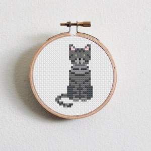 May include: A gray cat cross-stitch pattern on a round wooden embroidery hoop.