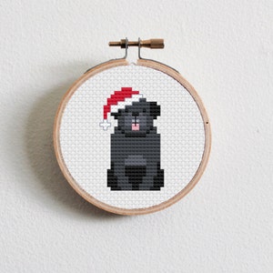 May include: A black dog wearing a red Santa hat, cross-stitched on a white fabric background. The dog is sitting with its tongue sticking out.