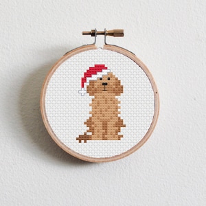 May include: A brown dog wearing a red Santa hat, cross-stitched on white fabric in a wooden embroidery hoop.