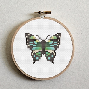 Puede incluir: Un aro de bordado de punto de cruz con un diseño de mariposa verde, azul y negra.