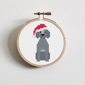 May include: A gray dog wearing a red Santa hat, cross-stitched on a round wooden hoop.