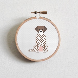 May include: A brown and white spotted dog cross stitch pattern in a wooden embroidery hoop.