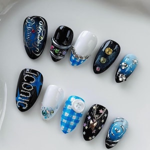 May include: A set of ten press-on nails featuring diverse designs including black, white, and blue color palettes. Embellishments include silver metallic accents, blue gingham patterns, rhinestones, star-shaped charms, and the text Iconic and Mistake.