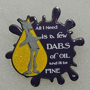May include: A purple and yellow enamel pin featuring a cartoon robot holding a yellow oil drop. The text on the pin reads "All I Need is a few DABS of OIL and I'll be FINE".