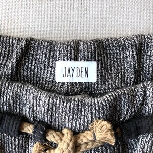 May include: Black and white knitted fabric with a white label that says "JAYDEN" on it. The fabric has a rope drawstring.