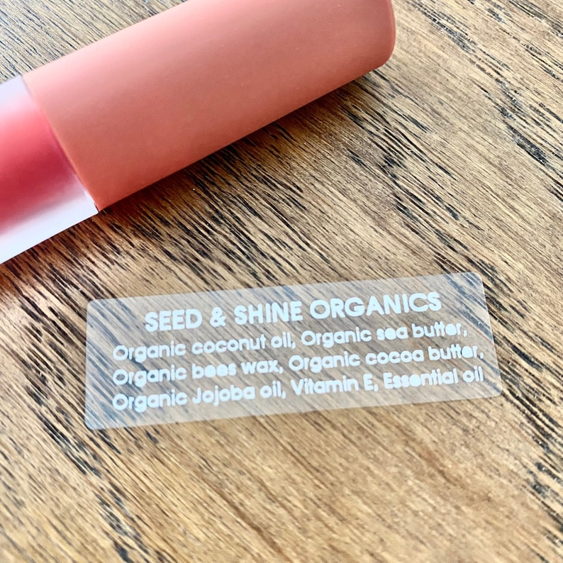 May include: A clear sticker with white text that reads "SEED & SHINE ORGANICS" and lists the ingredients: Organic coconut oil, Organic sea butter, Organic bees wax, Organic cocoa butter, Organic Jojoba oil, Vitamin E, Essential oil.