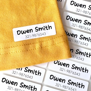 May include: White rectangular labels with the name "Owen Smith" and a phone number printed in black. One label is attached to a yellow top. More labels are visible in the background.