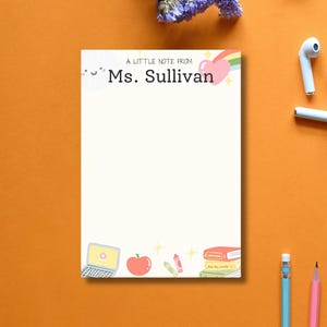 Peut inclure: Bloc-notes blanc avec l'inscription rose "A Little Note From Ms. Sullivan". Le bloc-notes est orné d'illustrations d'un ordinateur portable, d'une pomme, de crayons et de livres. Un arc-en-ciel et un cœur ornent le haut.