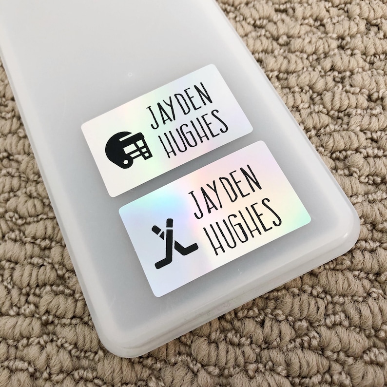 May include: Two iridescent white labels with black text and icons. The top label reads "JAYDEN HUGHES" with a football helmet icon. The bottom label reads "JAYDEN HUGHES" with a hockey stick icon.