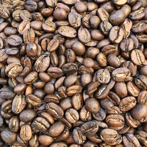 May include: A close-up view of a large quantity of roasted coffee beans. The beans are dark brown and have a shiny, oily surface.