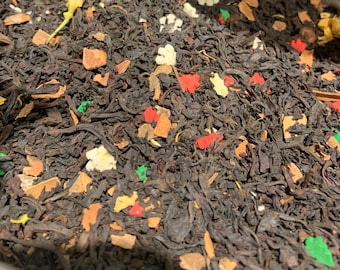 May include: Close-up of loose-leaf tea blend with dark brown tea leaves, and colorful pieces of fruit and spices. The blend includes red, green, and white pieces, along with brown cinnamon sticks and yellow flower petals.