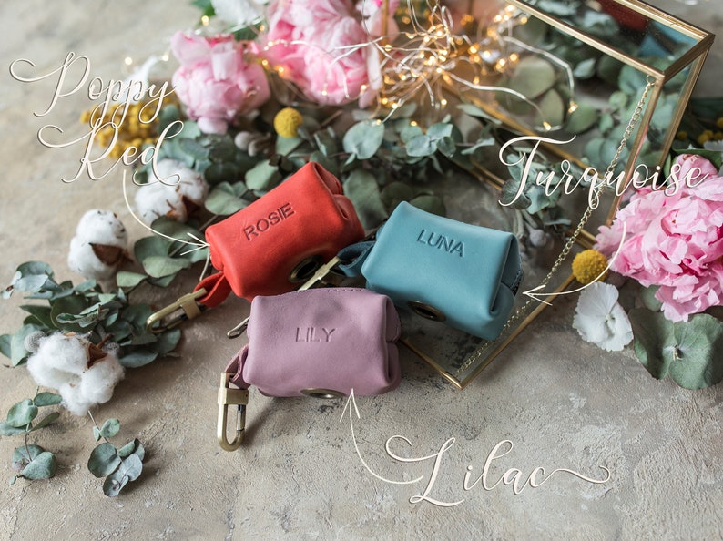 May include: Three small leather pouches with personalized names: Rosie, Luna, and Lily. The pouches are in red, turquoise, and lilac colors. The pouches are on a light brown surface with flowers and greenery.