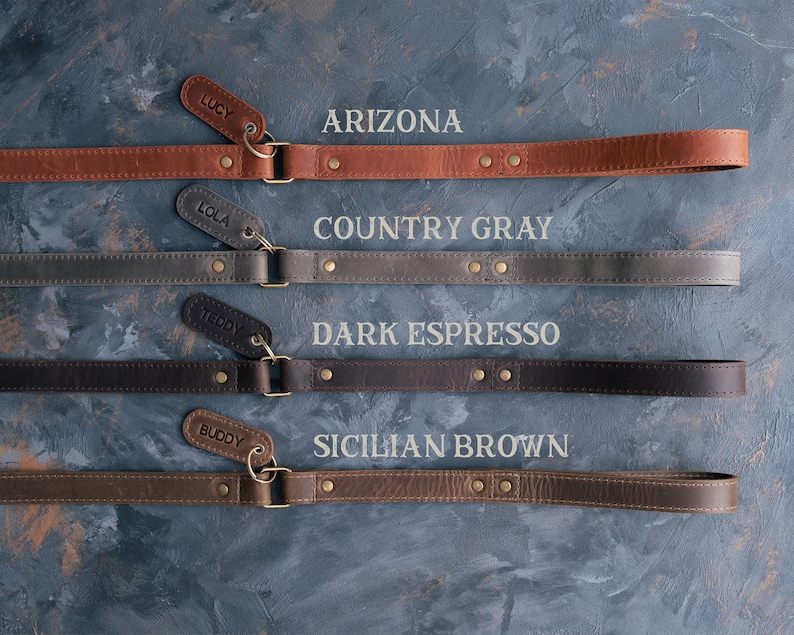 May include: Four leather dog leashes in different colors and textures, with the names "Lucy", "Lola", "Teddy", and "Buddy" on the tags. The leashes are labeled with the colors "Arizona", "Country Gray", "Dark Espresso", and "Sicilian Brown".