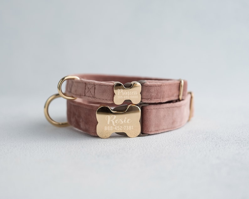 May include: Two pink velvet dog collars with gold bone-shaped tags. The top tag reads "Princess" with a phone number and the bottom tag reads "Rosie" with a phone number.