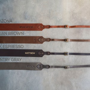 May include: Four leather camera straps in different colors: Arizona, Sicilian Brown, Dark Espresso, and Country Gray. Each strap has a brass buckle and a personalized name.