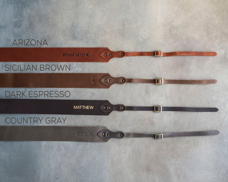 May include: Four leather camera straps in different colors: Arizona, Sicilian Brown, Dark Espresso, and Country Gray. Each strap has a brass buckle and a personalized name.