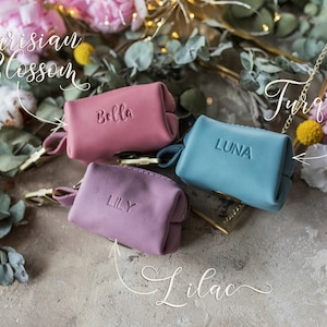 May include: Three small leather pouches with gold clasps and personalized names: Bella, Lily, and Luna. The pouches are in shades of pink and blue, with the text "Parisian Blossom", "Lilac", "Turquoise" written around them.