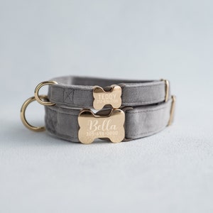 May include: Two gray velvet dog collars with gold bone-shaped tags. The top tag reads "Teddy 212-826-7700" and the bottom tag reads "Bella 305-696-0800".