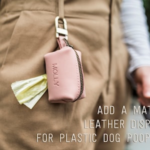May include: A pink leather dog poop bag dispenser with the word "MOLLY" embossed on the front. The dispenser is attached to a belt loop and has a yellow plastic poop bag sticking out of the top.