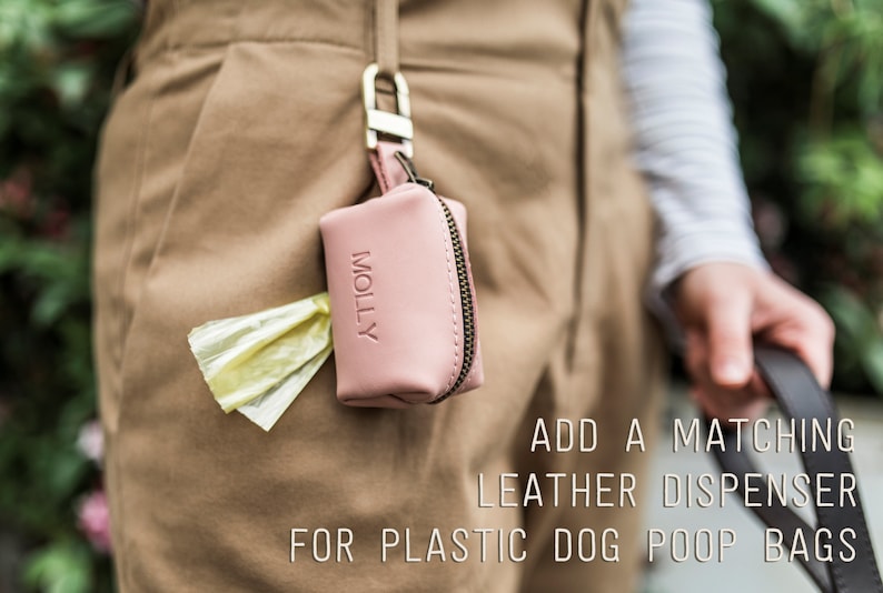May include: A pink leather dog poop bag dispenser with the word "MOLLY" embossed on the front. The dispenser is attached to a belt loop and has a yellow plastic poop bag sticking out of the top.