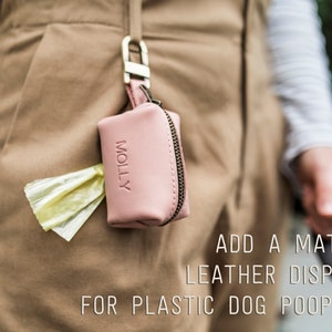 K&ouml;nnte beinhalten: Ein rosa Leder-Hunde-Kotbeutelspender mit dem Wort "MOLLY" auf der Vorderseite. Der Spender ist an einer G&uuml;rtelschlaufe befestigt und hat einen gelben Plastik-Kotbeutel, der oben herausragt.