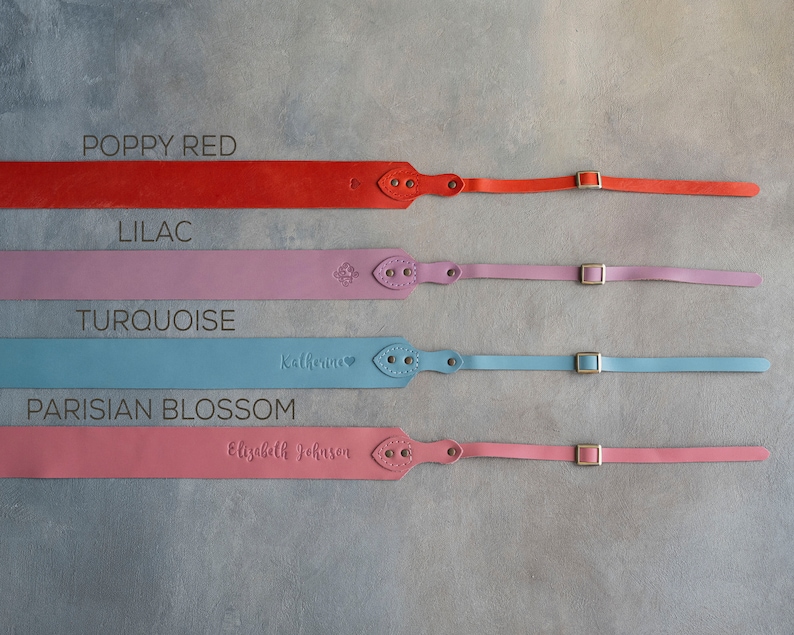 May include: Four leather camera straps in different colors: poppy red, lilac, turquoise, and Parisian blossom. Each strap has a gold buckle and a personalized name.