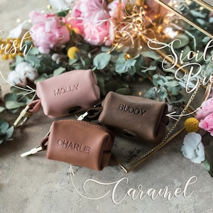 May include: Three small leather pouches with personalized names, "Molly", "Buddy", and "Charlie", in blush, caramel, and Sicilian brown colors. The pouches are surrounded by flowers and greenery.