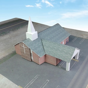 Peut inclure: Modèle d'une petite église avec un clocher blanc et un toit gris. L'église est en papier et a une façade en briques roses et brunes. L'église est posée sur une surface grise avec une route et un parking en arrière-plan.