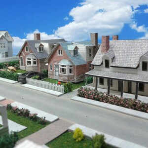 May include: A model of a suburban street with four houses, two cars, and a white picket fence. The houses are all different styles and colors, and the street is paved with asphalt.