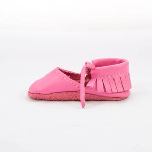 May include: Pink leather baby moccasins with fringe detail. The moccasins have a soft, flexible sole and a comfortable fit.