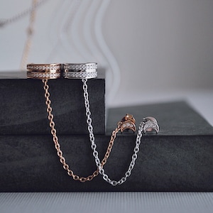 May include: Three pairs of silver and gold earrings with dangling chains. The earrings are adorned with small, clear gemstones.