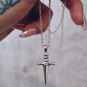Pode incluir: Um colar de corrente de prata com um pingente de adaga de prata. A adaga tem uma pedra em forma de diamante no centro e &eacute; detalhada com pequenos acentos redondos.