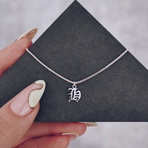 Puede incluir: Un collar de cadena de plata con un colgante de plata en forma de la letra "B" en una fuente inglesa antigua.