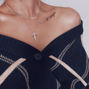 Pode incluir: Um colar de corrente de prata com um pingente de espada. O colar tem 45,7 cm de comprimento e &eacute; usado por uma pessoa com um cardigan listrado preto e branco.