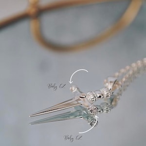Pode incluir: Colar com pingente de prata com design de espada com pedras de zirc&ocirc;nia c&uacute;bica transparentes. O pingente est&aacute; em uma corrente de prata.