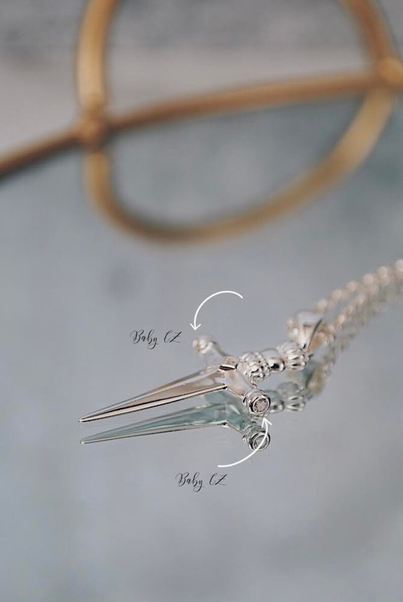 Pode incluir: Colar com pingente de prata com design de espada com pedras de zirc&ocirc;nia c&uacute;bica transparentes. O pingente est&aacute; em uma corrente de prata.