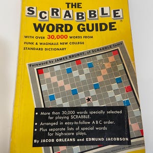 May include: A vintage Scrabble Word Guide book with a yellow cover. The cover features the title in large, bold letters and includes information about the number of words and the publisher. The book also includes a Scrabble board graphic.