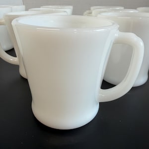 May include: A set of three ceramic mugs with a speckled, matte finish. The mugs are in shades of cream, light brown, and dark brown. Each mug has a simple, minimalist design and a rounded handle. The mugs are likely for coffee or tea.