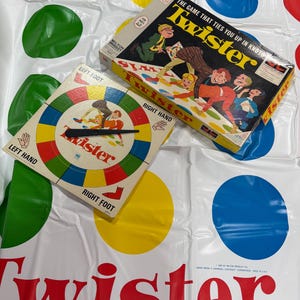 May include: A Twister board game set including a large white plastic mat with rows of red, yellow, green, and blue circles, a square cardboard game box with vintage illustrations, and a circular spinner board with four colored sections.