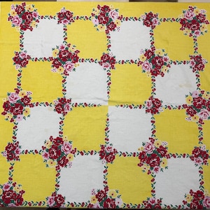 May include: A vintage tablecloth with a yellow and white checkered pattern. The yellow squares are bordered by a floral design of red and pink roses with green leaves. The tablecloth has a white border.