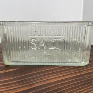 May include: A clear glass salt container with a ribbed design and the word "SALT" embossed on the front.