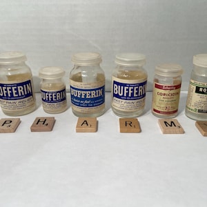 May include: Six vintage medicine bottles with blue and white labels. The bottles are arranged in a row on a wooden surface. The labels include the names "Bufferin", "Coricidin", and "Robaxin".