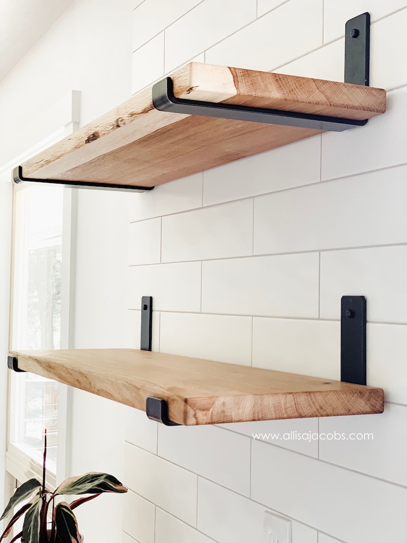 Bright modern kitchen with two oak wood shelves wall mounted on white tile backsplash with heavy duty black shelf brackets. The shelves are empty. There is small text ©allisajacobs