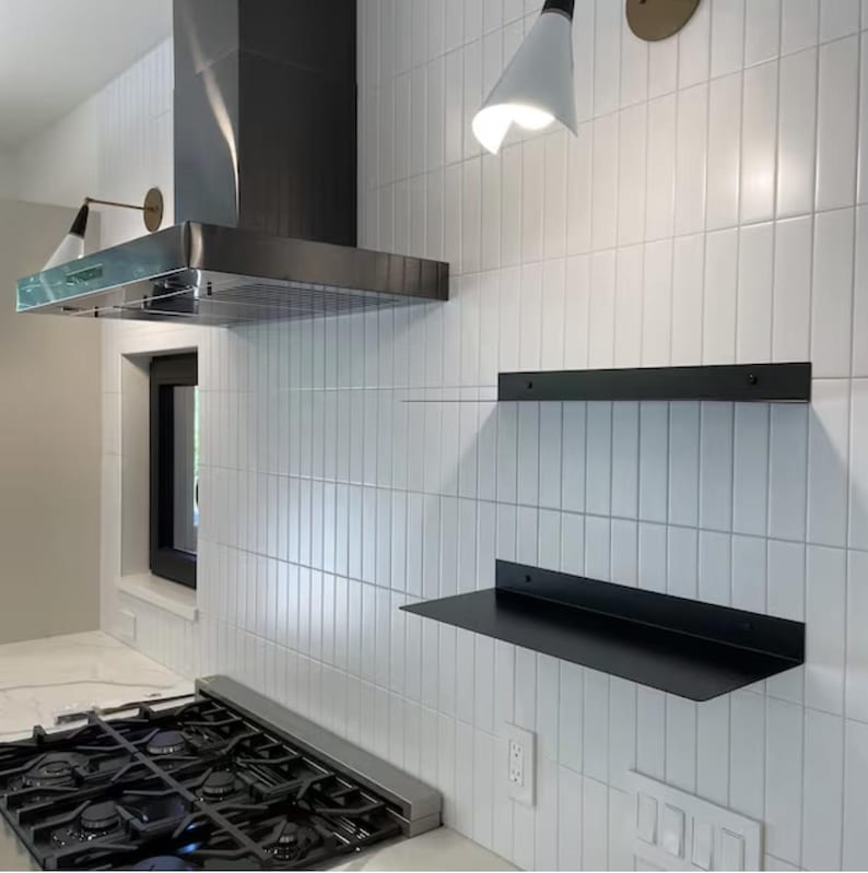 Two black metal shelves mounted on a white tiled wall in a kitchen. The shelves are empty and ready to be styled.