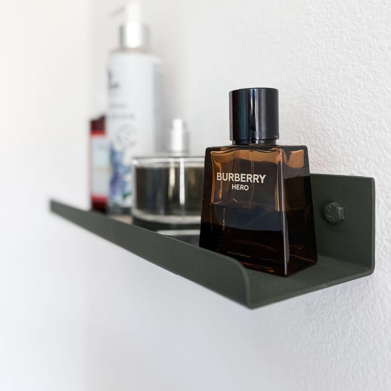 Bathroom with a small dark green metal shelf ledge mounted on a white wall with lotion bottles and cologne being displayed