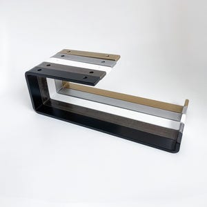 Five under mount metal paper towel holders with open arm and front lip lined up in black, white, silver, brass, steel