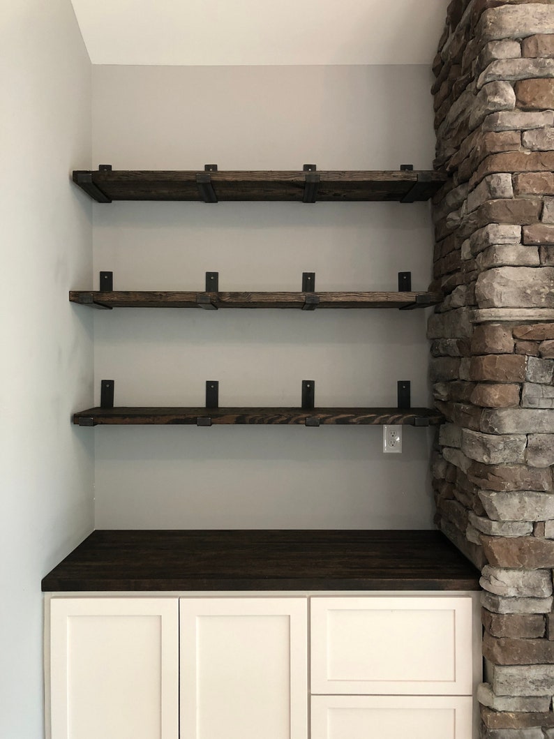 bar nook with three dark wood shelves supported by heavy duty metal shelf brackets next to a fireplace